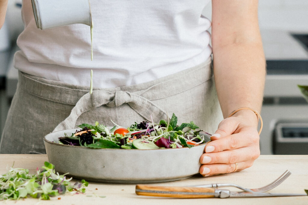 Salad dressing is being poured onto a prepared salad, bringing the viewer's attention to the details of the image.