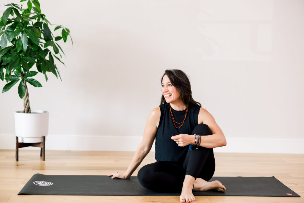 Yoga studio owner sat on a mat, smiling to the side.