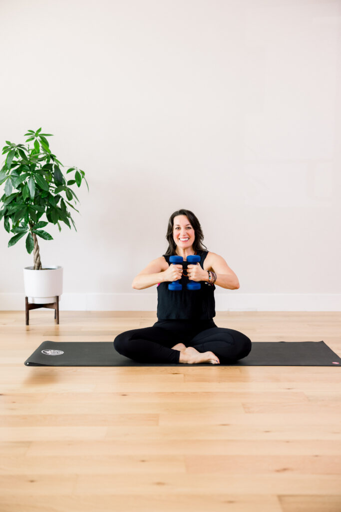 A Pilates instructor sat on a yoga mat with blue hand weights during a brand photo shoot.