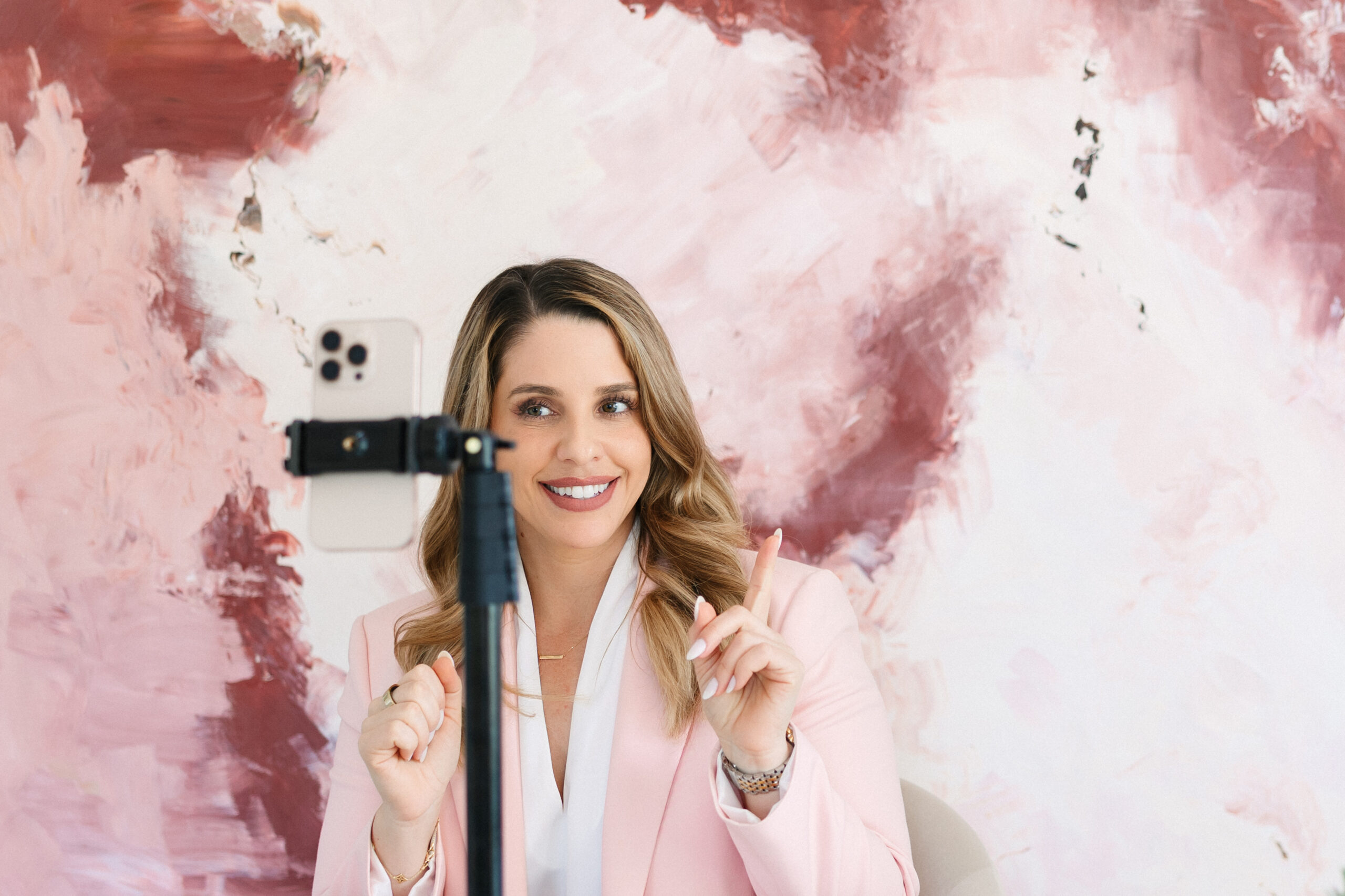 A woman demonstrating an example of"The uniform" look and smiling at an iPhone on a tripod, while creating content for social media.