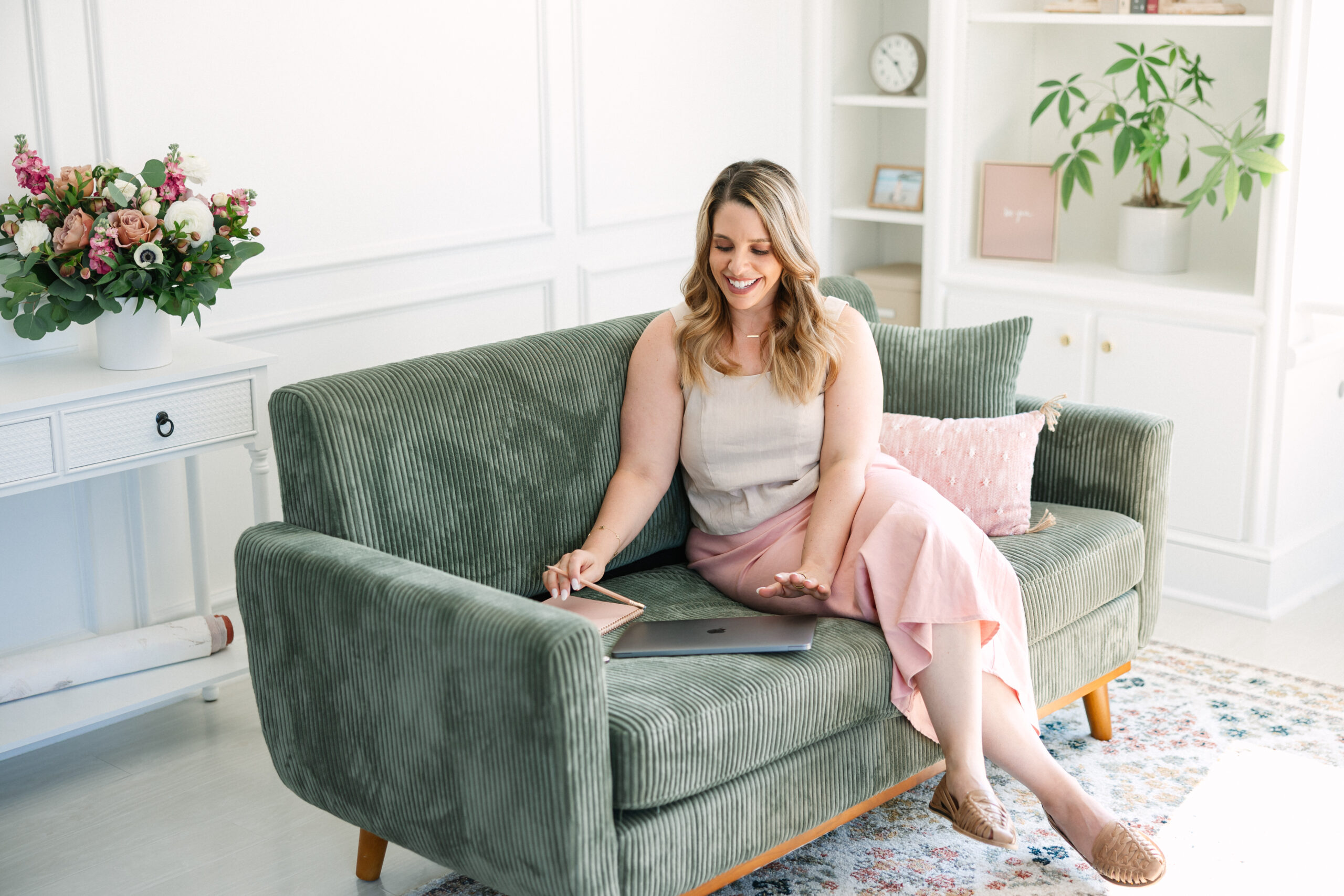 A woman sat on a green sofa closing a lap top