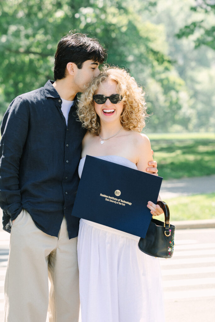 a graduate with her boyfriend kissing her head as she holds her diploma