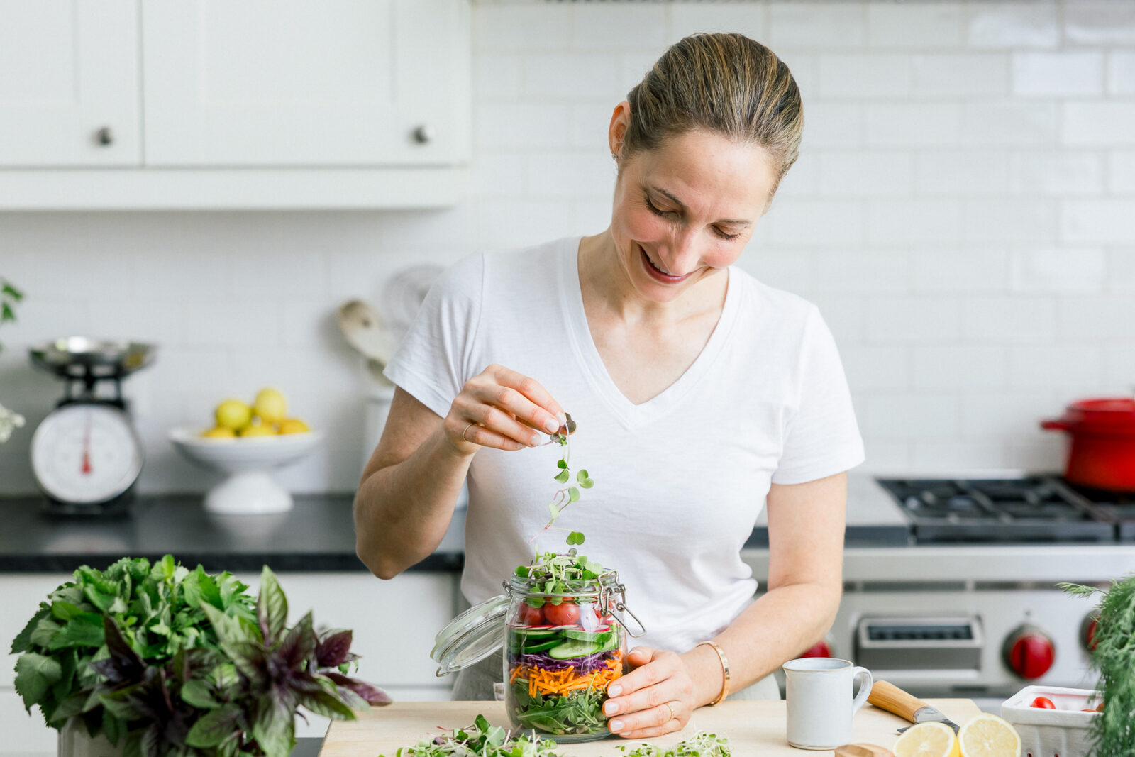 A wellness coach sprinkling micro-greens into a mason jar packed with vibrant vegetables.