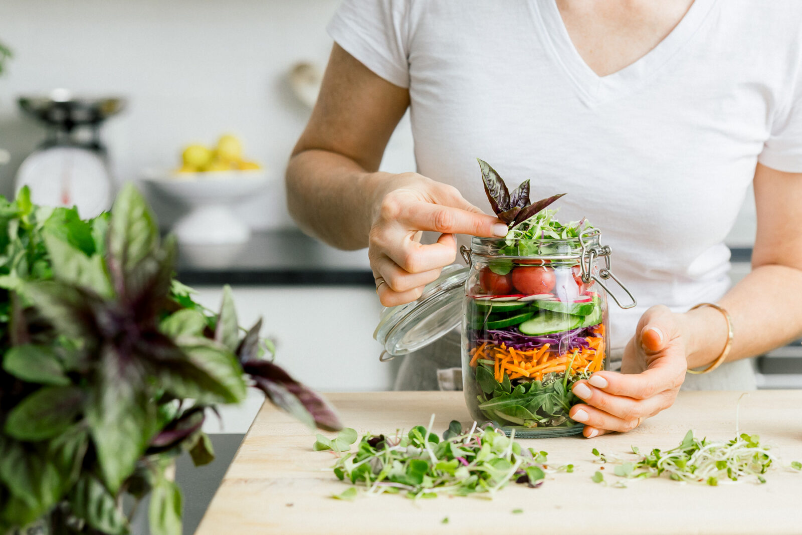 Wellness coach placing a sprig of purple basil on top of a mason jar full of fresh vegetables.