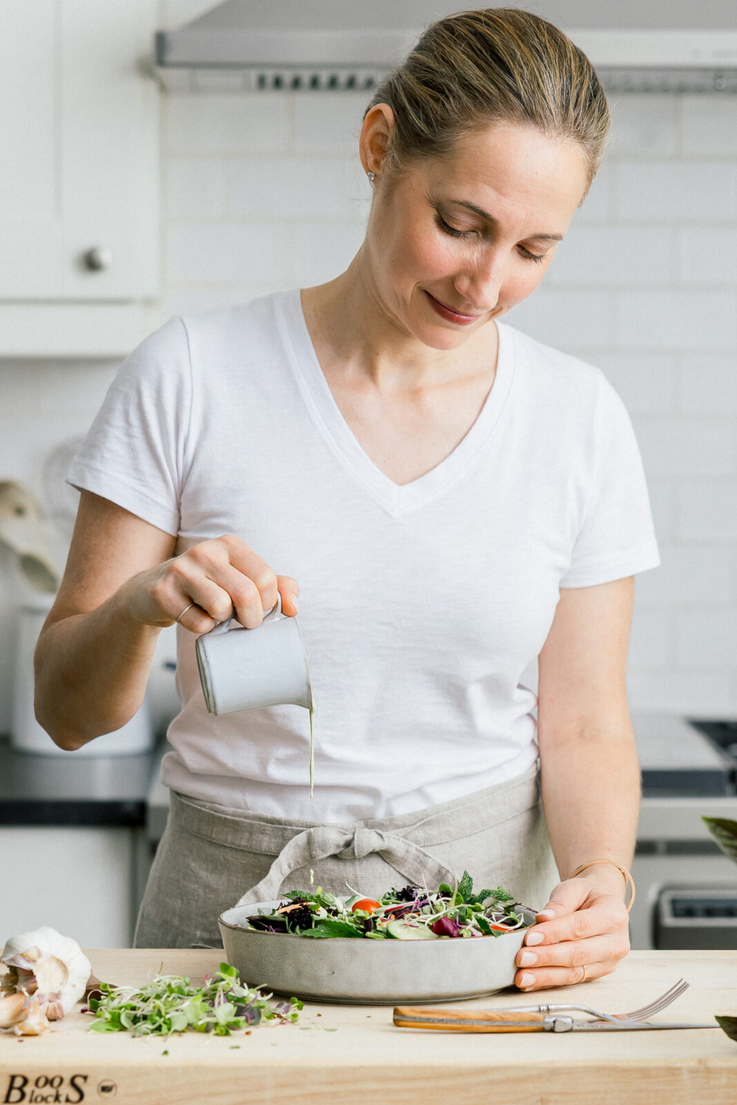 A wellness coach is pouring dressing onto a salad in a ceramic bowl.