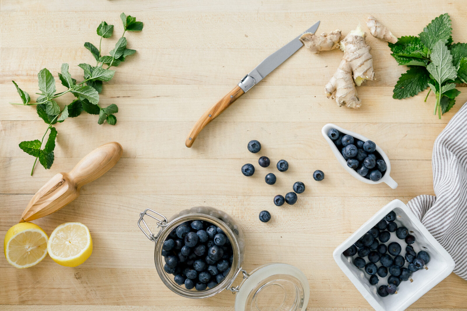 Blueberries, mint leaves, fresh ginger root, and a halved lemon on a wooden cutting board.