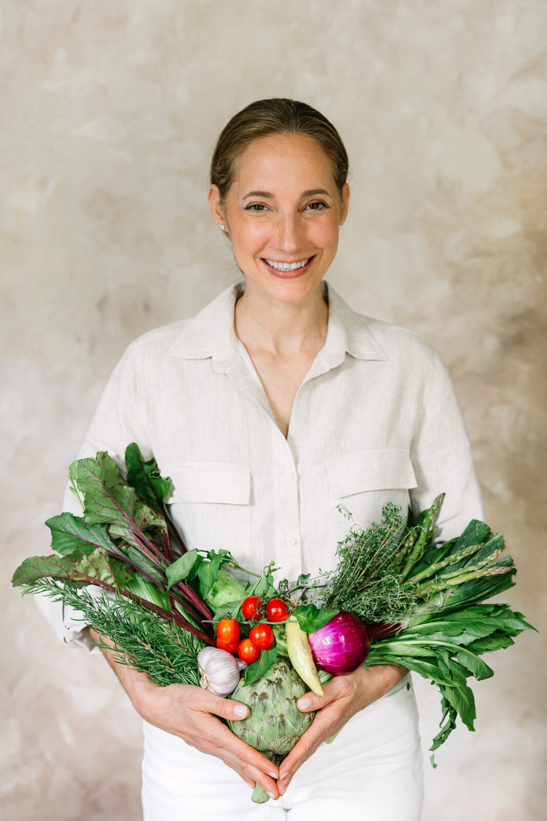 A wellness coach holding lots of vibrant, colorful vegetables in her arms.