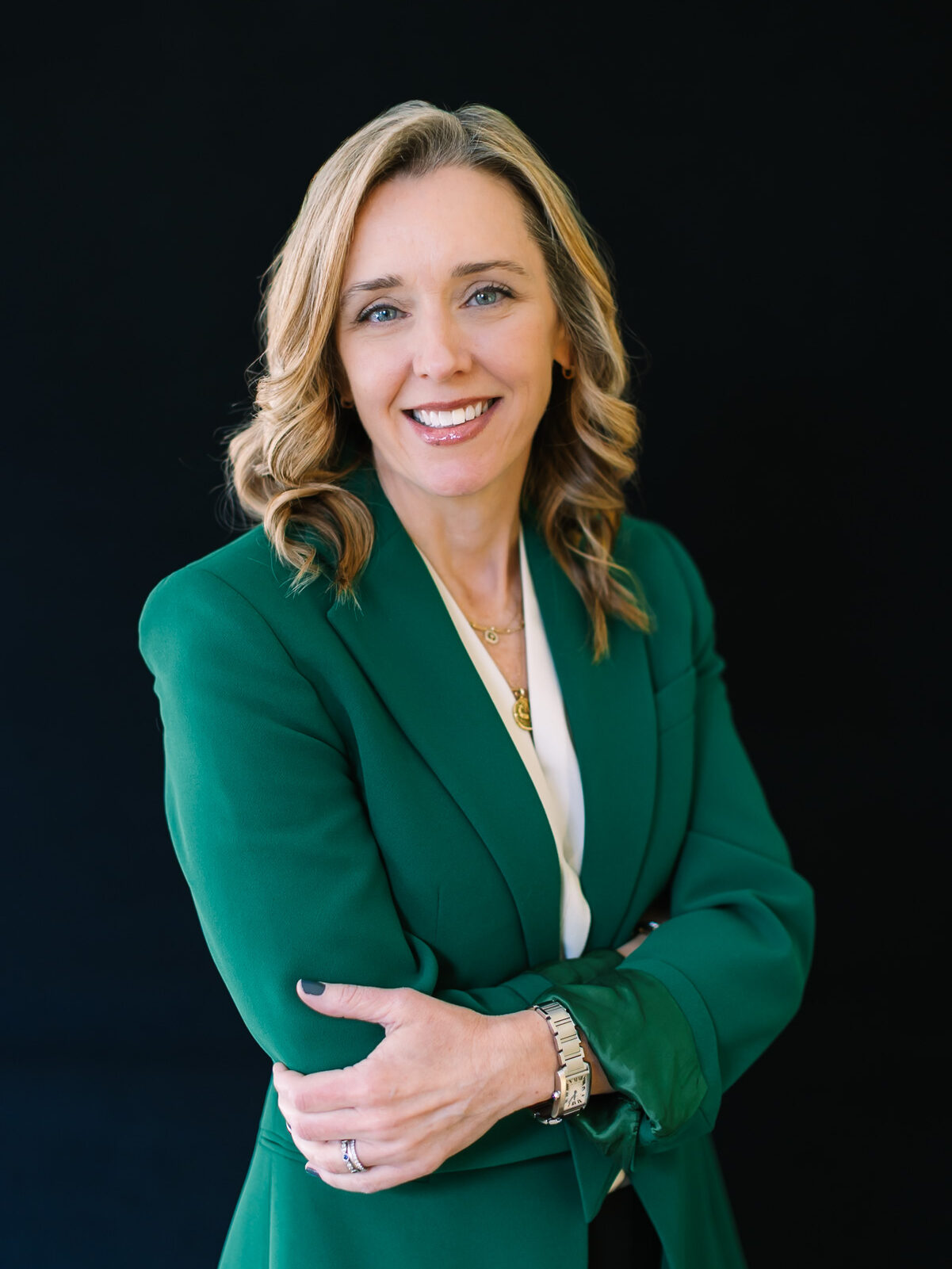 Professional headshot of a businesswoman wearing a green blazer against a black background.